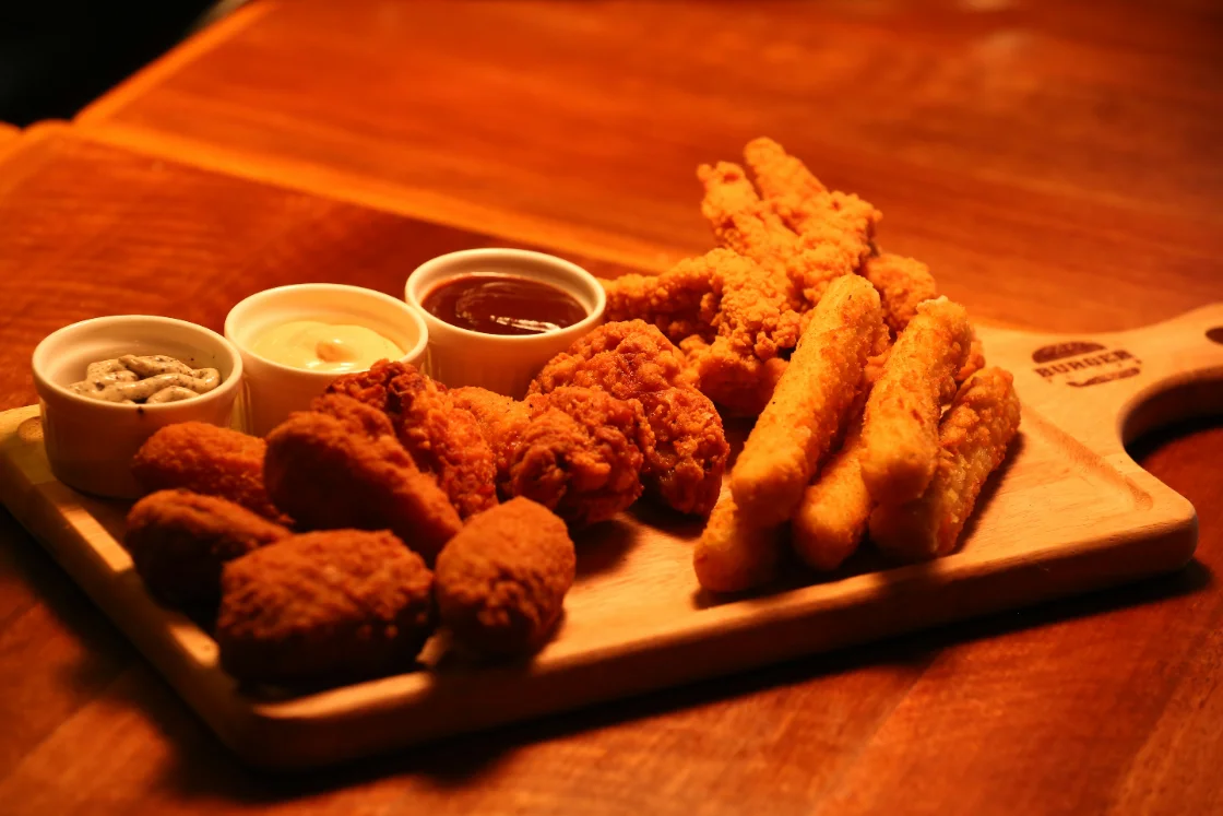 Een plank met kroketten, nuggets en kipfingers met bakjes saus